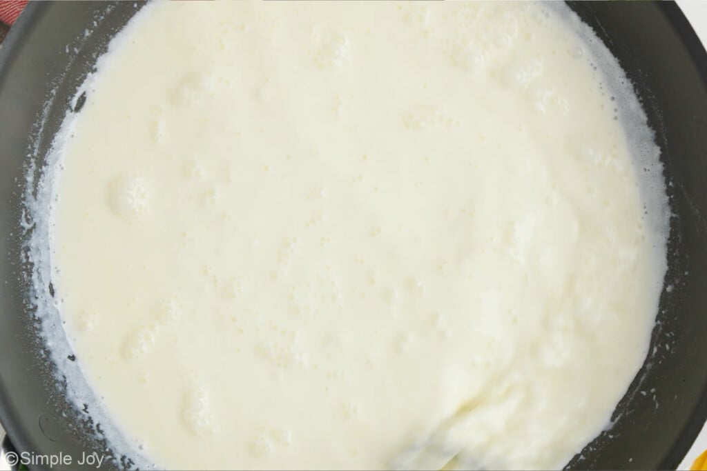 overhead of skillet of fettuccine alfredo sauce with bubbles while simmering. - 6