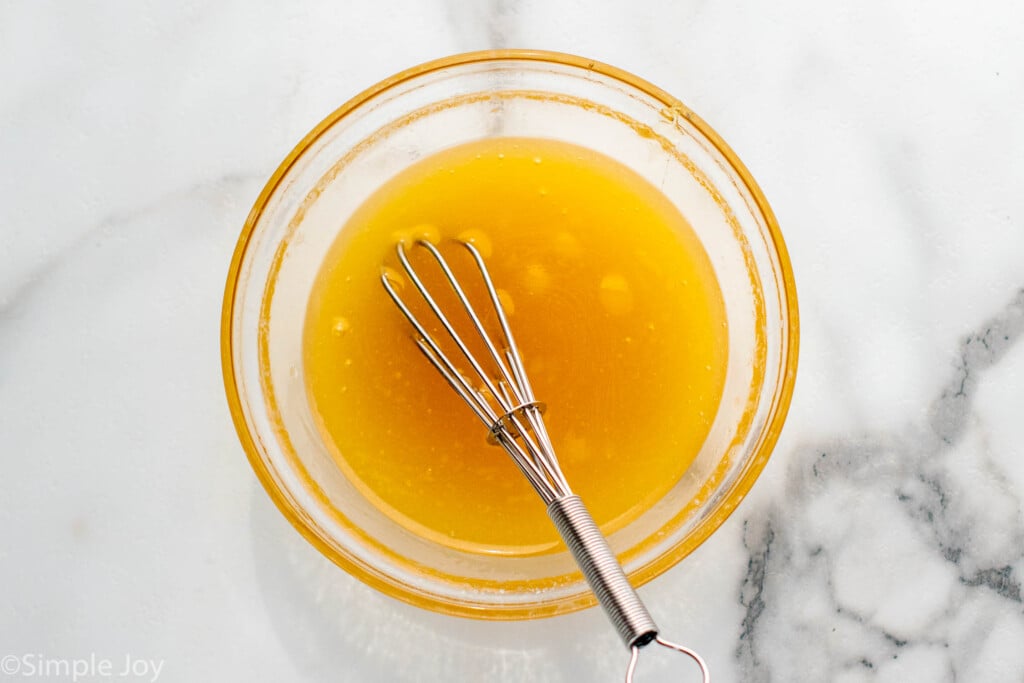 Overhead view of a mixing bowl of glaze with a whisk for Honey Roasted Carrots recipe.