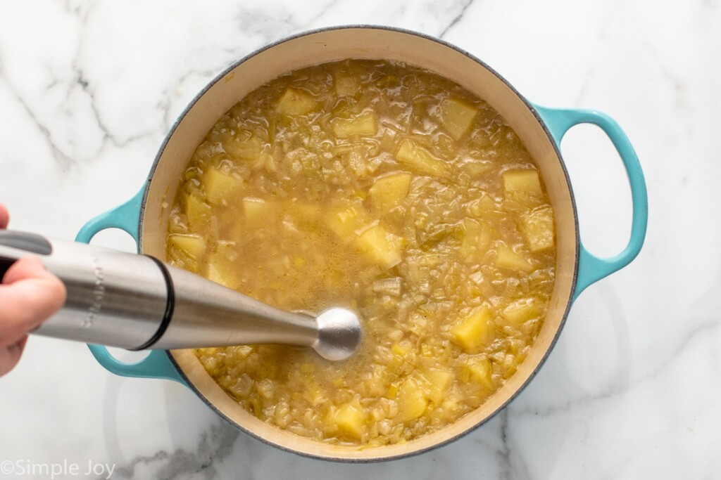 Overhead view of a pot of potato leek soup recipe with immersion blender. - 7