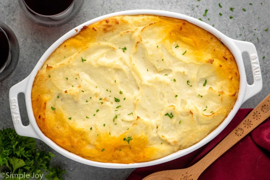 Overhead view of baking dish of Shepherd's Pie with glasses of red wine and a spoon beside - 11