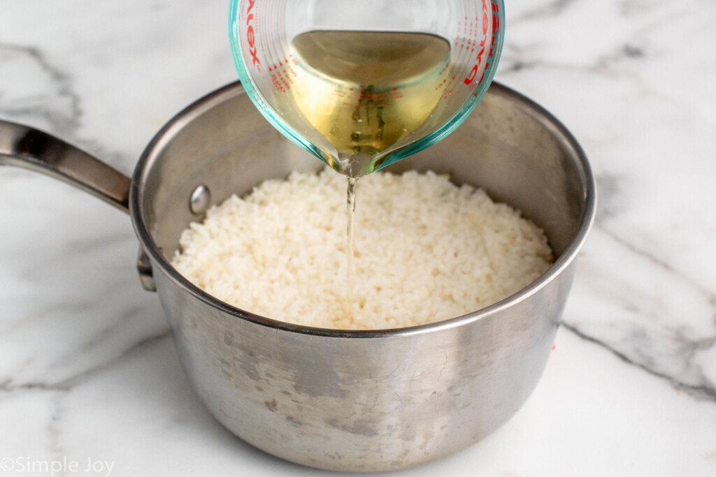 Measuring cup of liquid being poured over saucepan of rice for Sushi Bowl recipe. - 5
