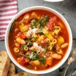 Overhead view of bowls of minestrone soup with bread and spoons beside - 13