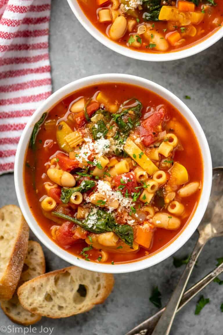 Overhead view of bowls of minestrone soup with bread and spoons beside