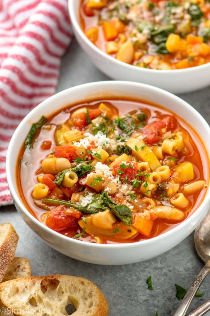 Bowls of minestrone soup with bread and spoons beside - 3