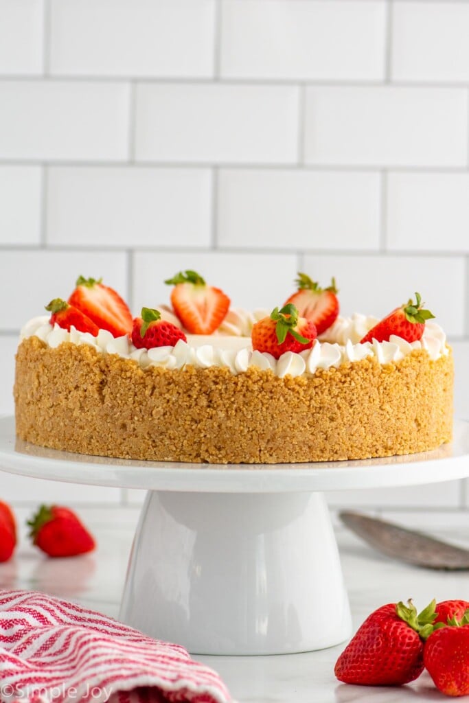 Side view of No Bake Cheesecake served on a cake plate garnished with strawberries. Strawberries on counter beside. - 6