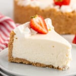 Slice of No Bake Cheesecake garnished with whipped cream and a strawberry served on a plate, No Bake Cheesecake beside. - 16
