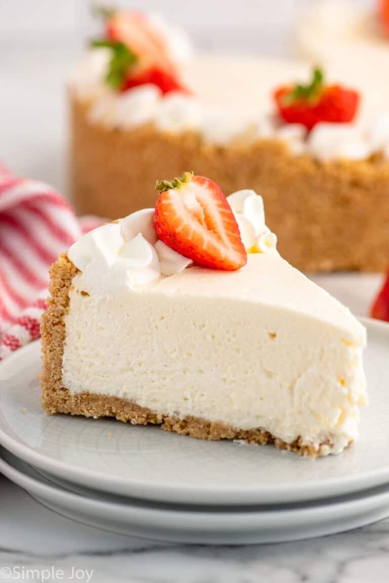 Slice of No Bake Cheesecake garnished with whipped cream and a strawberry served on a plate, No Bake Cheesecake beside.