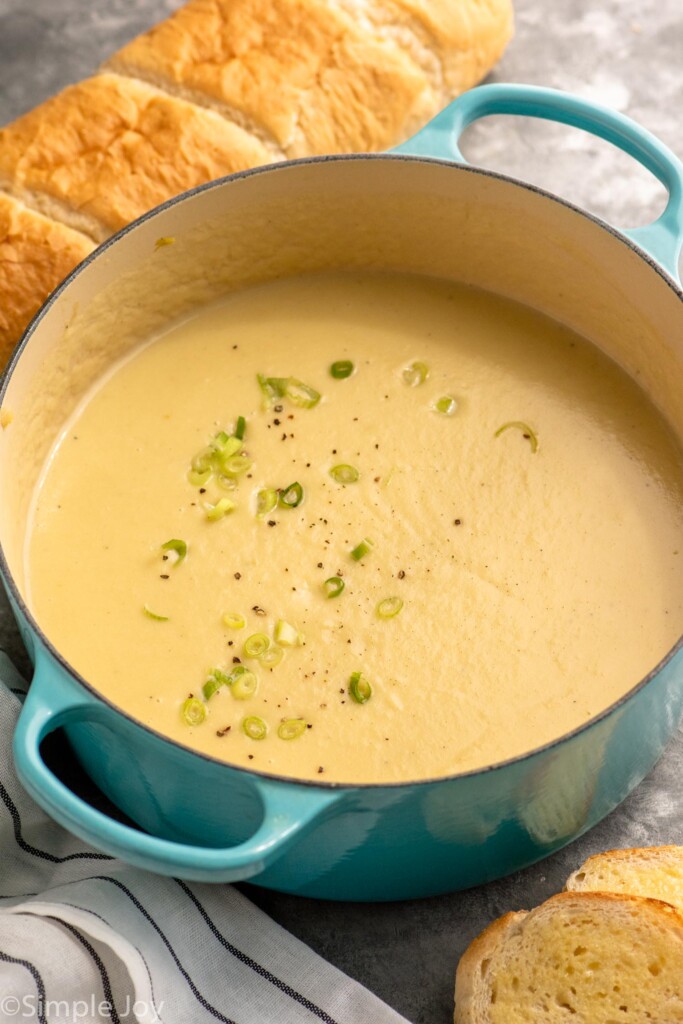Pot of potato leek soup garnished with pepper and chopped green onions, bread beside. - 8