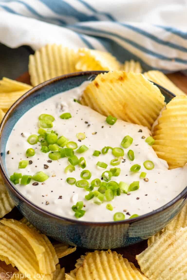Bowl of Clam Dip garnished with chopped green onions with potato chips