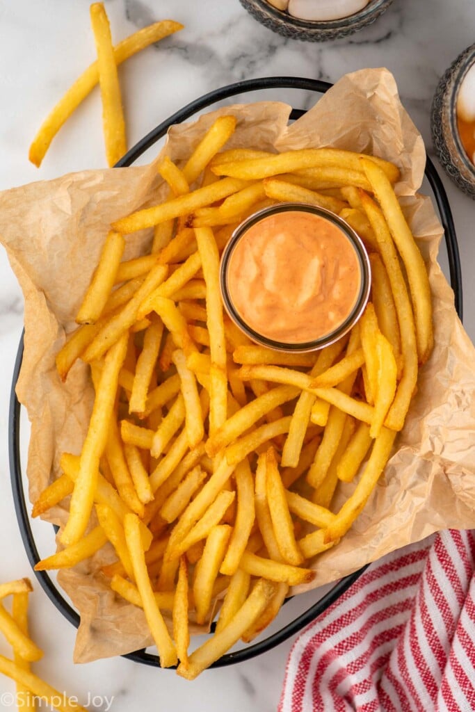 Overhead view of a basket of french fries with a cup of Sriracha Mayo - 5