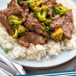 Pinterest graphic for easy Beef and Broccoli recipe. Image shows a plate of rice topped with easy Beef and Broccoli, garnished with sesame seeds and chopped green onions. Text says, "beef and broccoli simplejoy.com."