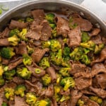 Pinterest graphic for easy Beef and Broccoli recipe. Text says, "the best Beef and Broccoli simplejoy.com." Image shows overhead view of a skillet of easy Beef and Broccoli garnished with sesame seeds and chopped green onions.