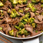 Pinterest graphic for easy Beef and Broccoli recipe. Image shows a skillet of easy Beef and Broccoli topped with chopped green onions and sesame seeds. Text says, "25 minute beef and broccoli simplejoy.com."