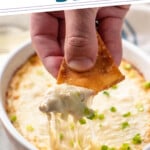 Pinterest graphic for crab rangoon dip recipe. Text says, "the best crab rangoon dip simplejoy.com." Image shows person's hand pulling pita chip out of crab rangoon dip garnished with chopped green onions.