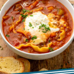 Pinterest graphic for Lasagna Soup recipe. Image shows a bowl of Lasagna Soup with bread and glass of red wine beside. Text says, "Lasagna Soup simplejoy.com."