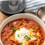 Pinterest graphic for Lasagna Soup recipe. Text says, "the best Lasagna Soup simplejoy.com." Image shows bowl of Lasagna Soup with bread, glass of red wine, and spoons beside.