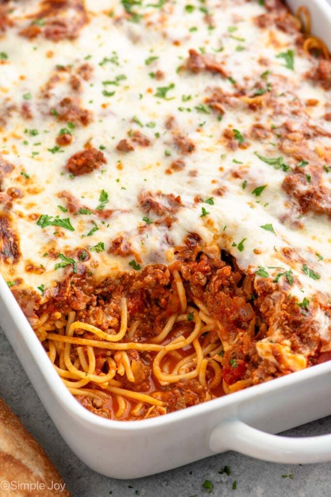 Baking dish of Baked Spaghetti with piece missing, garnished with parsley.