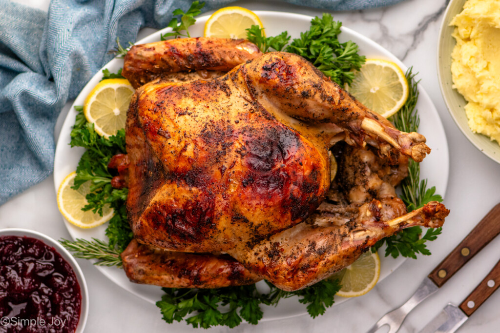 Baked turkey made with turkey brine recipe on a platter garnished with lemon slices and greens.