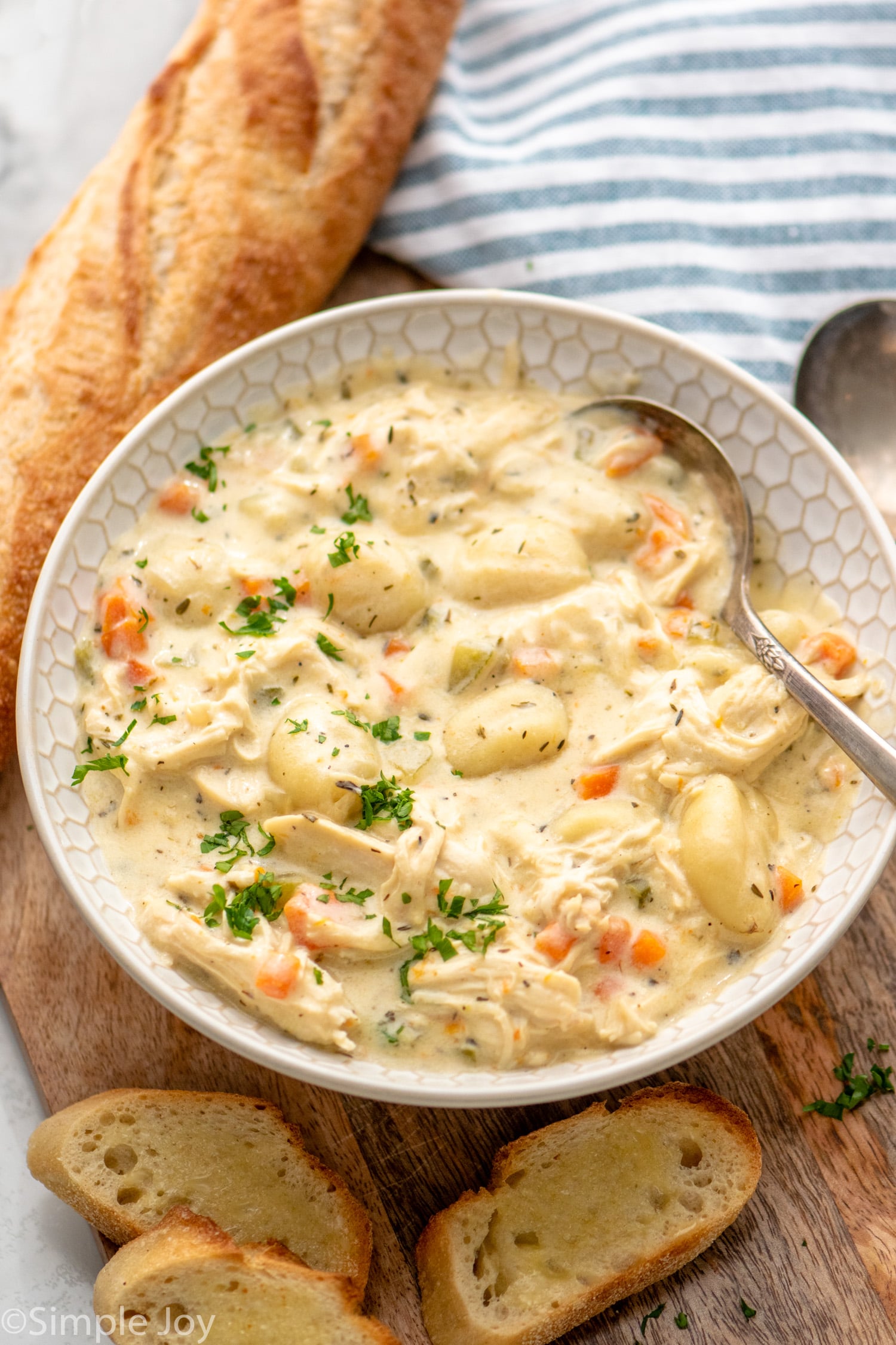 Bowl of chicken gnocchi soup with spoon. Bread beside.