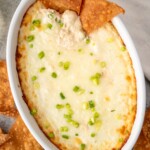 Baking dish of crab rangoon dip garnished with chopped green onions, pita chips in and beside - 10