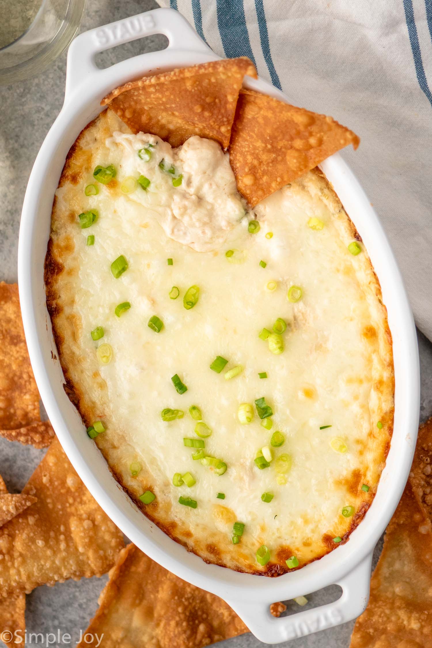 Baking dish of crab rangoon dip garnished with chopped green onions, pita chips in and beside