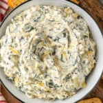 Overhead view of a bowl of Crockpot Spinach Artichoke Dip with toasted bread slices beside. - 10