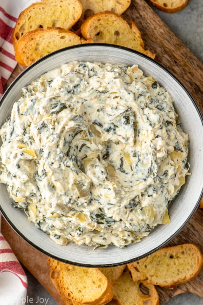 Overhead view of a bowl of Crockpot Spinach Artichoke Dip with toasted bread slices beside. - 8