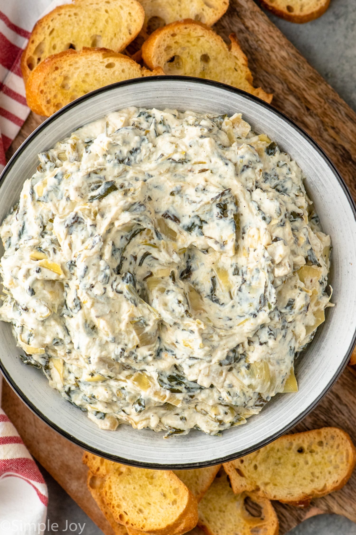 Overhead view of a bowl of Crockpot Spinach Artichoke Dip with toasted bread slices beside. - 5