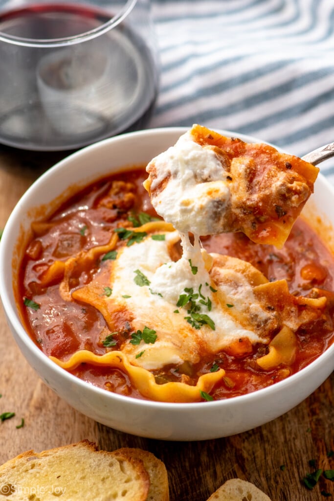 Bowl of Lasagna Soup with spoon lifting up a bite. Bread and glass of red wine beside.