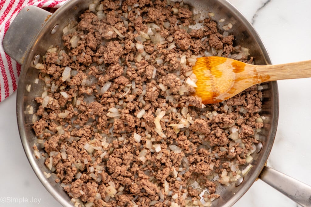 Overhead view of a skillet of browned hamburger and onions with a spoon for Baked Spaghetti recipe.