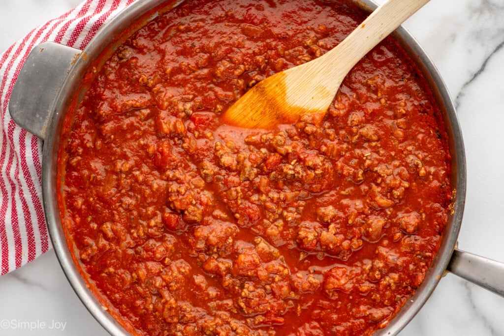 Overhead view of a skillet of meat sauce with wooden spoon for Baked Spaghetti recipe/