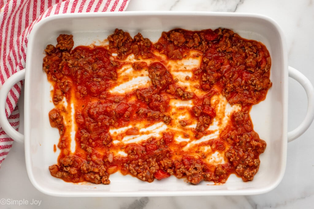 Overhead view of a baking dish with meat sauce on the bottom for Baked Spaghetti recipe.
