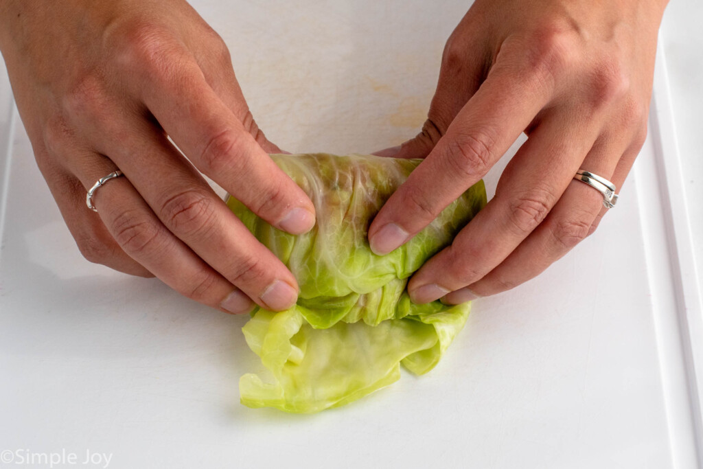 Close up view of person's hands rolling up cabbage roll for Stuffed Cabbage Rolls recipe.
