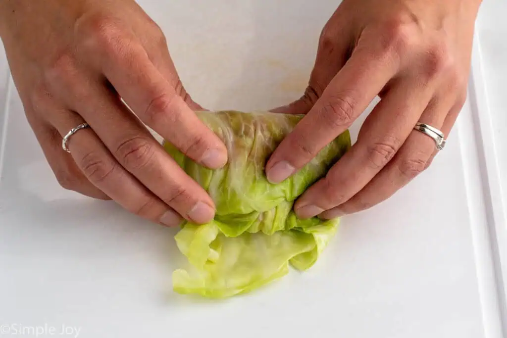Close up view of person's hands rolling up cabbage roll for Stuffed Cabbage Rolls recipe.