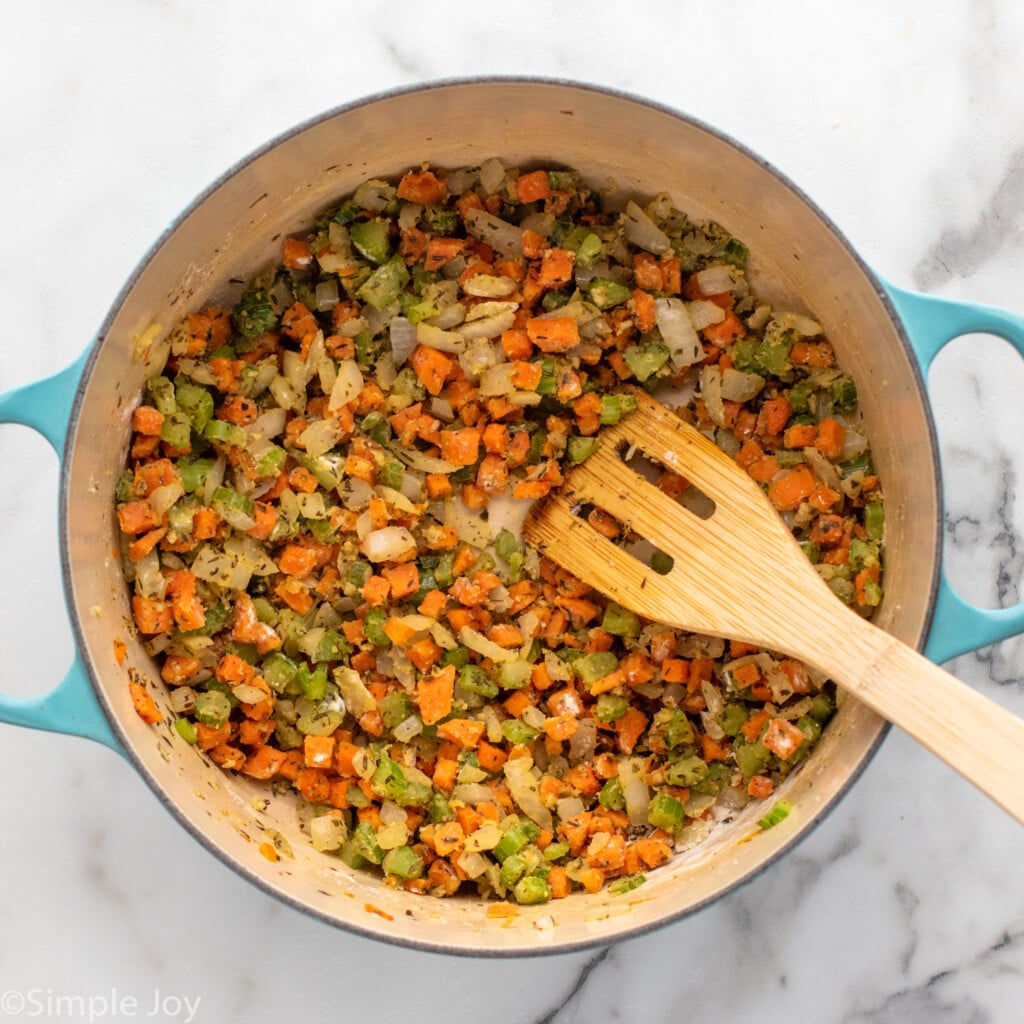 Overhead view of a pot of chopped vegetables and seasons with wooden spoon for chicken gnocchi soup recipe.