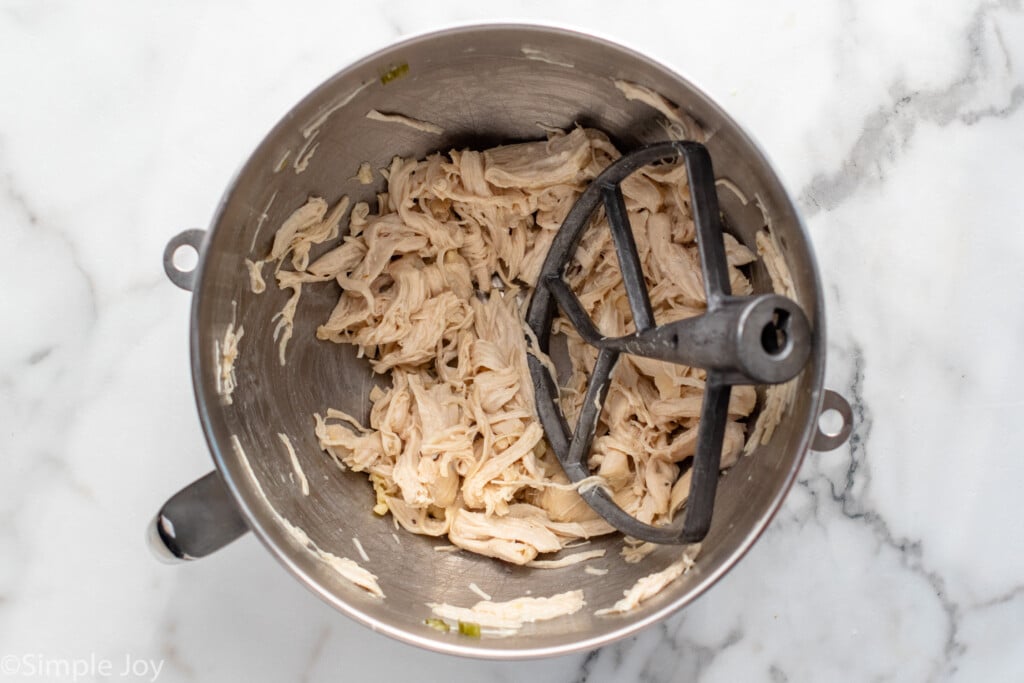 Overhead view of a mixing bowl and beaters with shredded cooked chicken.