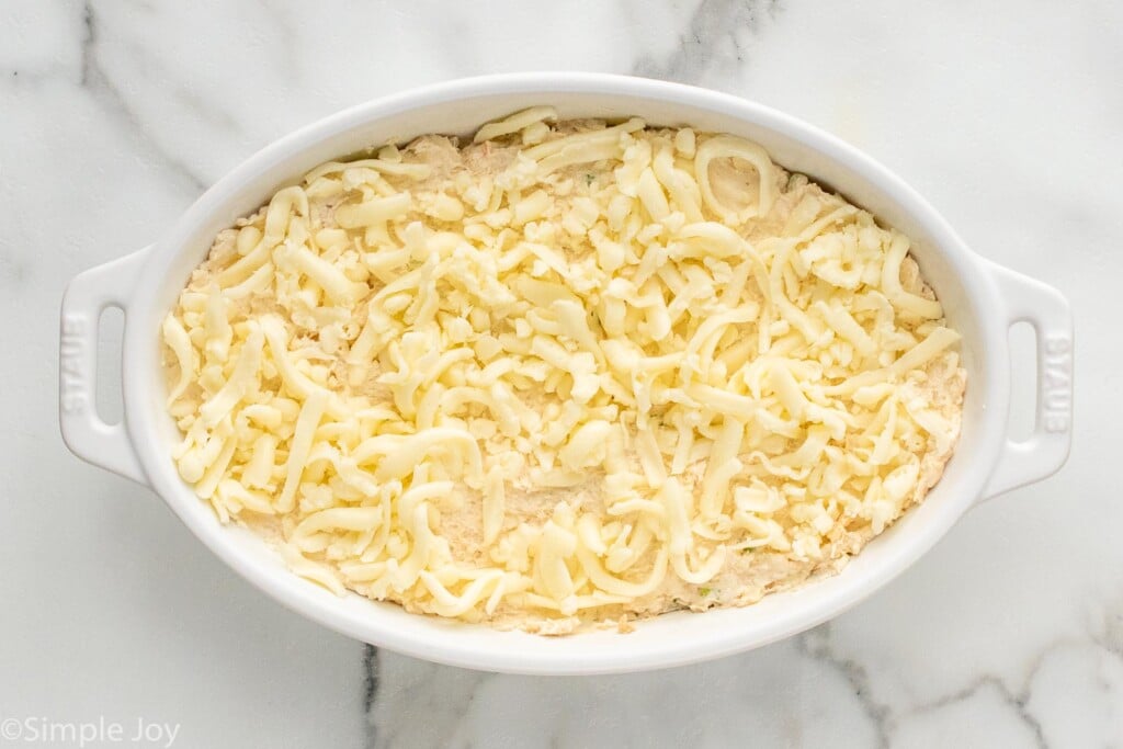 Overhead view of a baking dish of crab rangoon dip recipe topped with shredded cheese before baking - 7