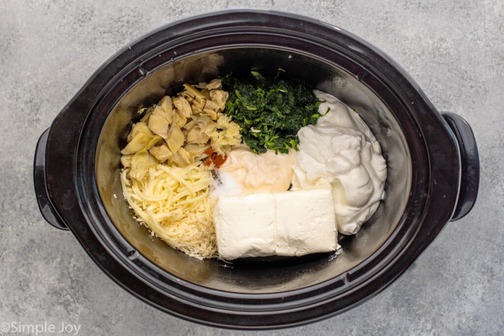 Overhead view of a crockpot with ingredients for Crockpot Spinach Artichoke Dip recipe. - 6