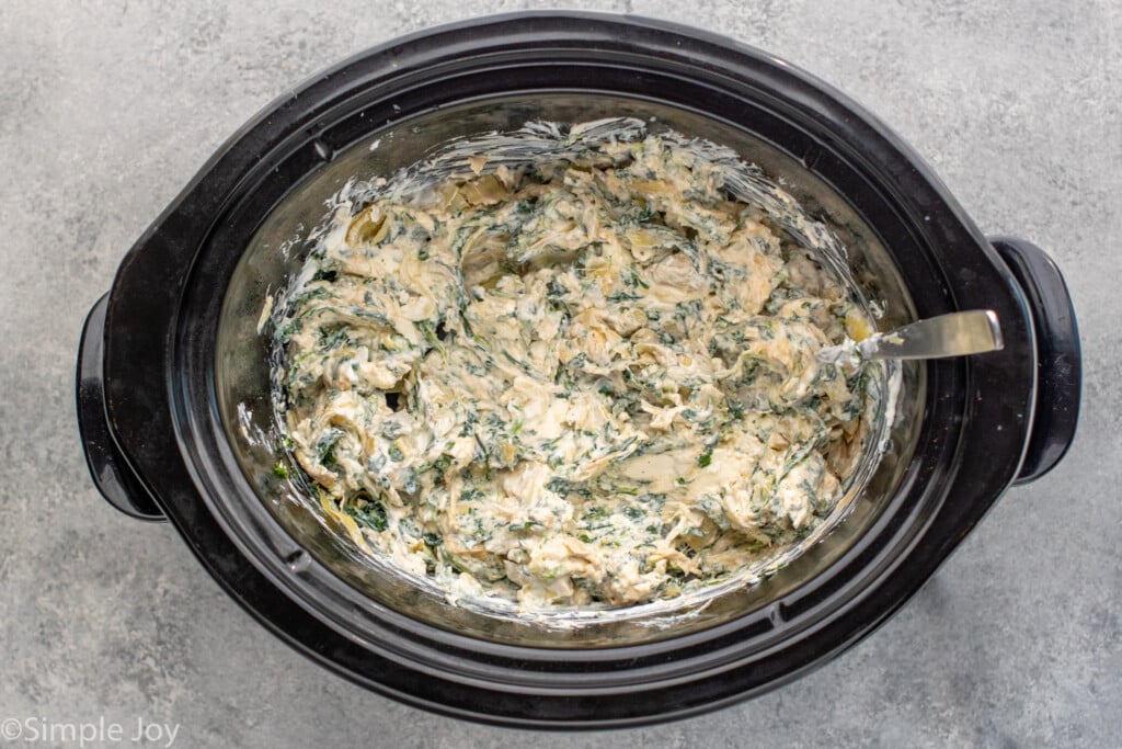 Overhead view of a crockpot with Crockpot Spinach Artichoke Dip recipe mixed together with a spoon.