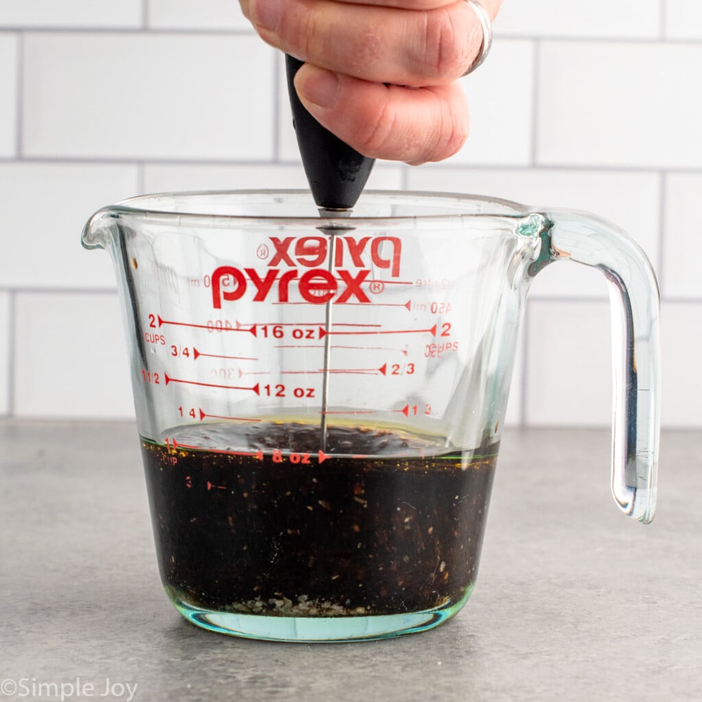 Side view of a a glass measuring cup of Winter Salad dressing with an immersion blender mixing it.