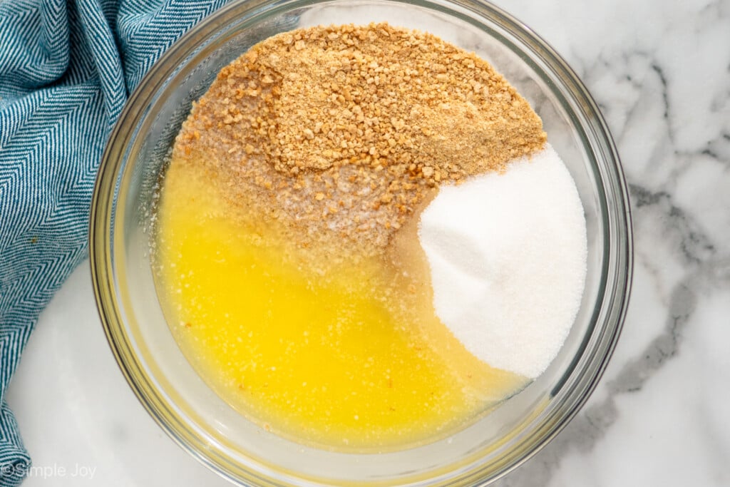 Overhead view of ingredients for graham cracker crust recipe in a clear mixing bowl before mixing - 7