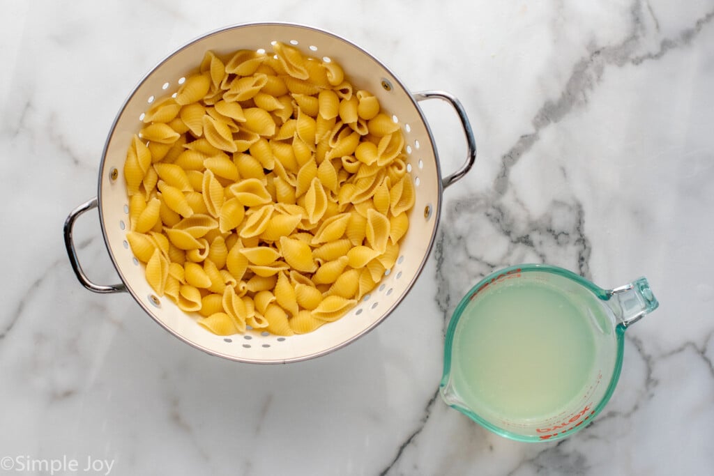 Overhead view of shell noodles in a colander and a glass measuring cup of pasta water for Sausage Broccoli Pasta recipe. - 5
