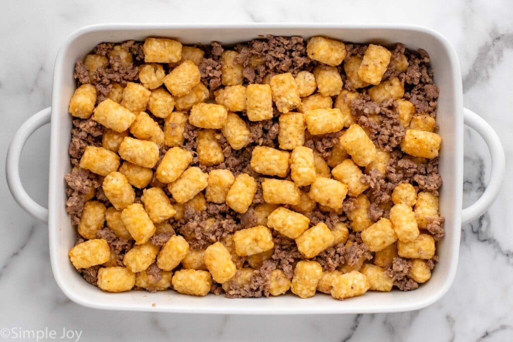 Overhead view of a baking dish of tater tots and ground sausage for tater tot breakfast casserole recipe.