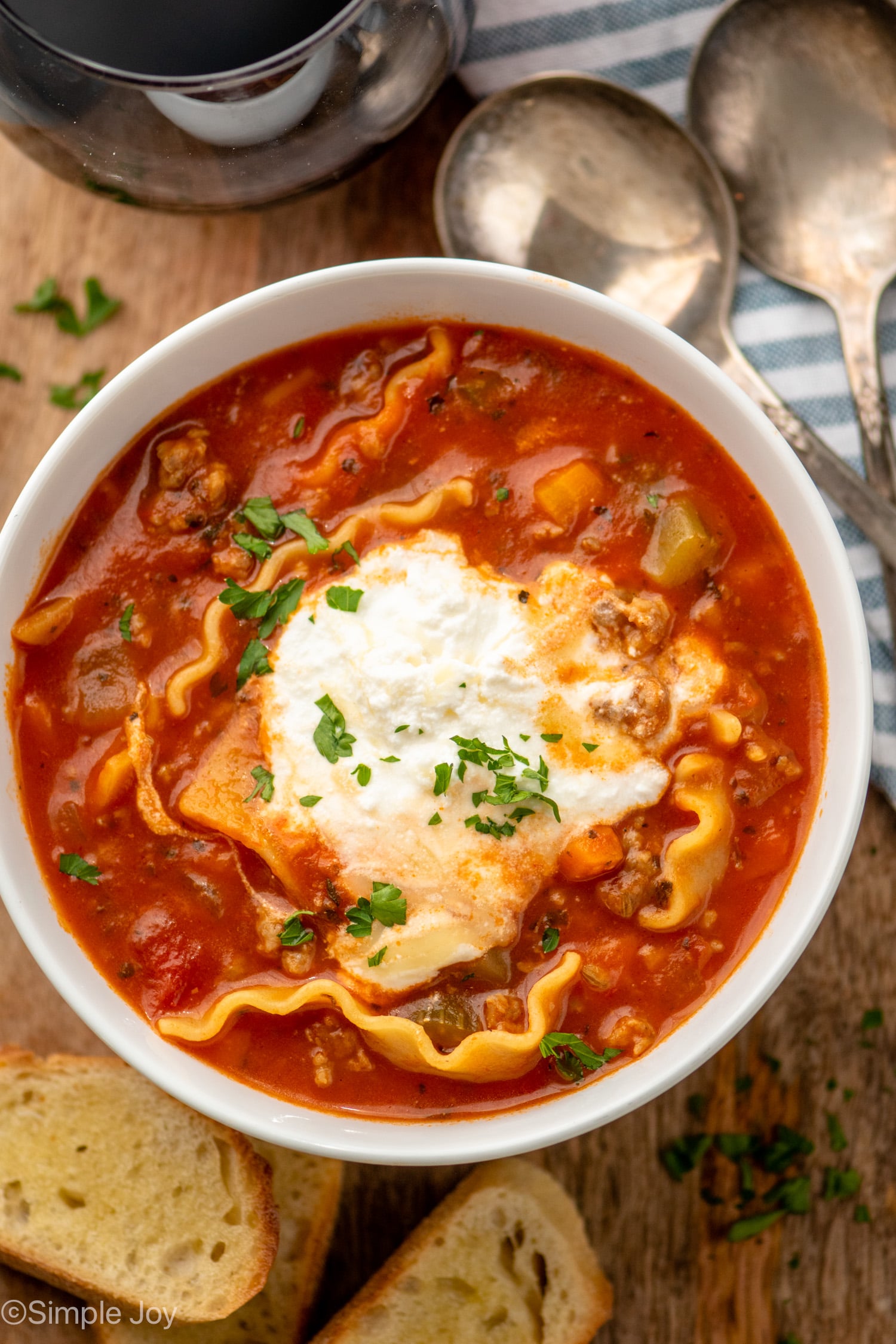 Overhead view of a bowl of Lasagna Soup with bread and spoons beside.