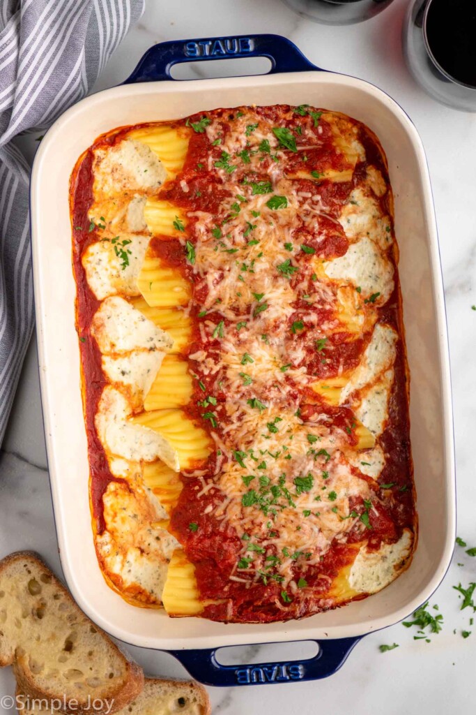 Overhead view of a baking dish of Cheese manicotti garnished with parsley flakes with bread beside