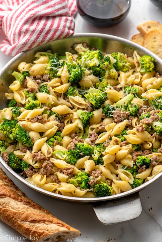 Skillet of Sausage Broccoli Pasta with bread and glass of red wine beside. - 10