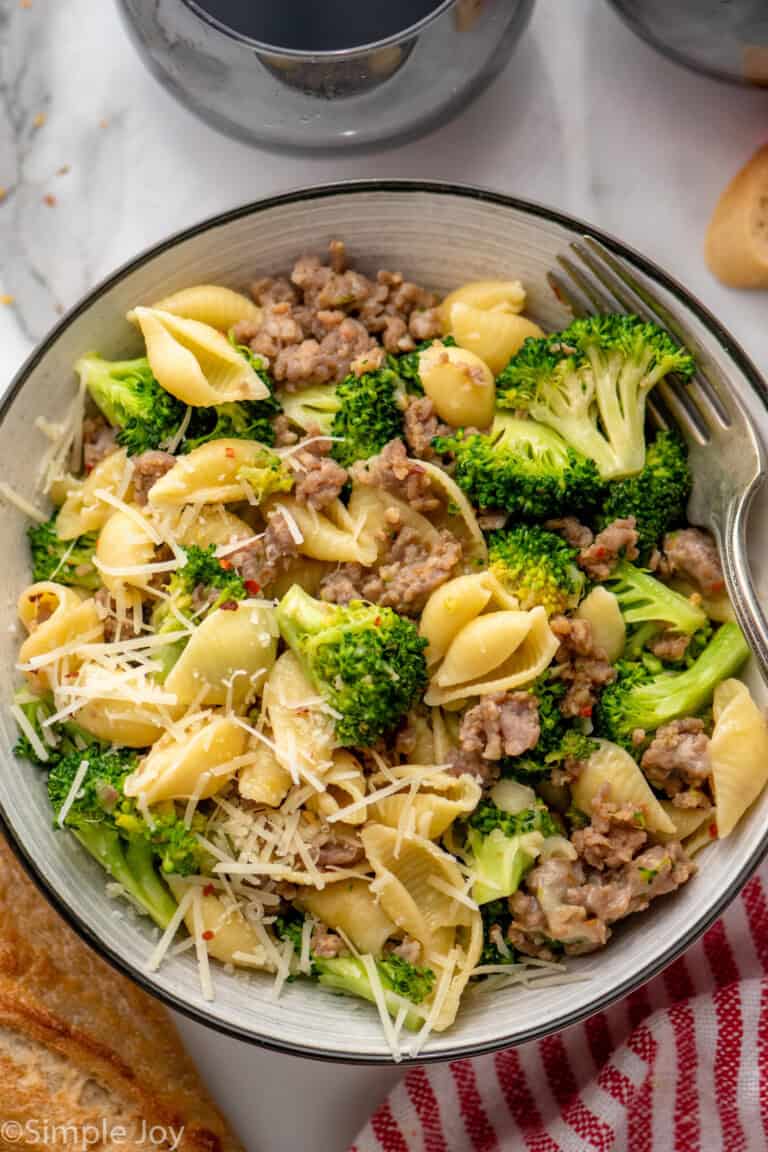 Overhead view of a bowl of Sausage Broccoli Pasta garnished with parmesan cheese with a fork. Glass of red wine beside.