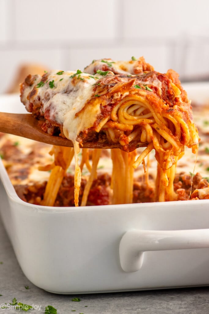 Side view of of a serving spoon serving a portion of Baked Spaghetti from baking dish.