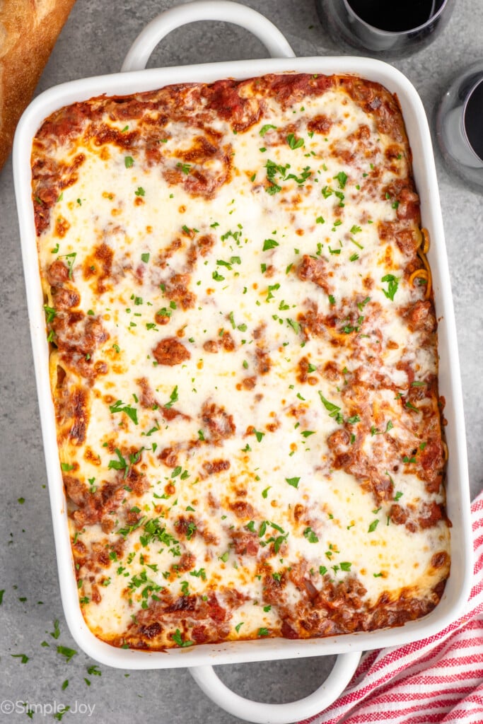 Overhead view of a baking dish of Baked Spaghetti with glasses of red wine beside.
