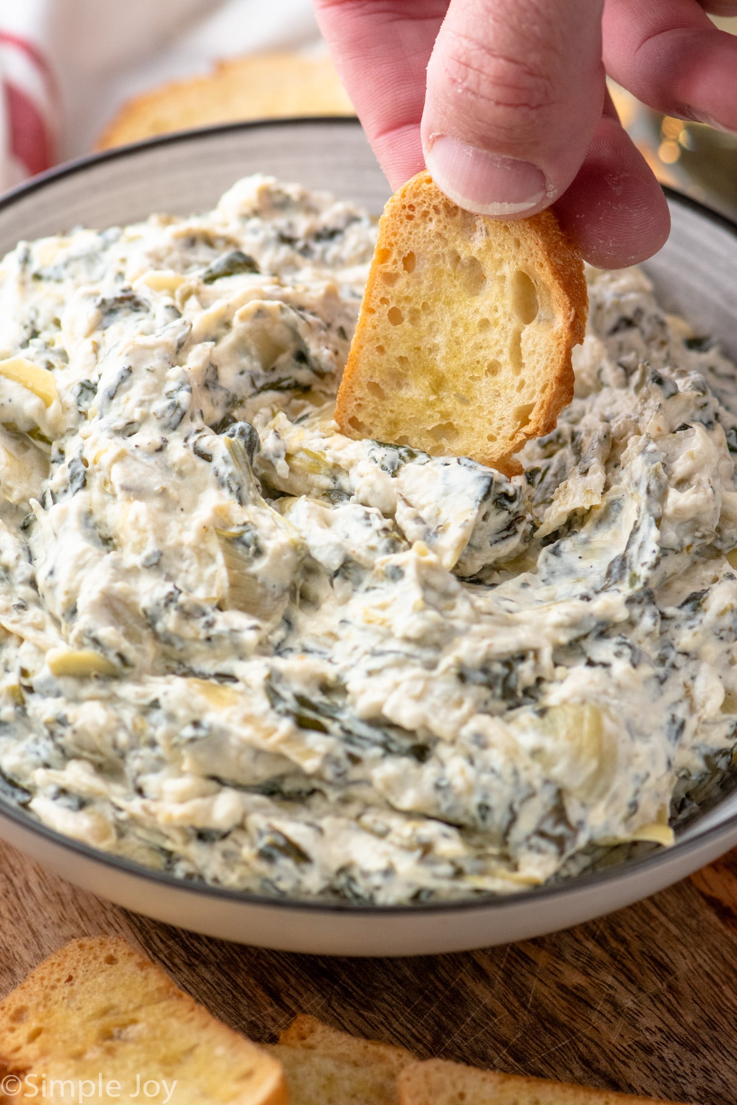 Person's hand dipping toasted bread into Crockpot Spinach Artichoke Dip